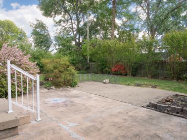 A spacious backyard with a concrete patio and lush greenery.