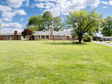 Spacious lawn with a ranch-style house and trees under a blue sky.
