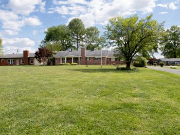 A single-story brick house with a large grassy front yard and trees.