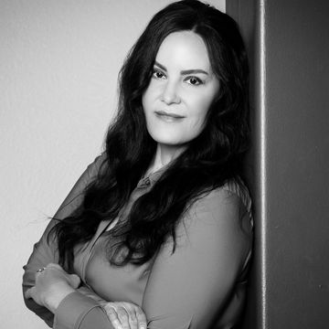 Black and white portrait of a confident woman leaning against a wall.