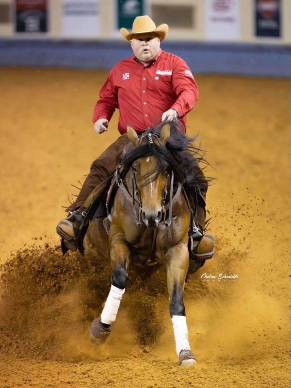 Man in cowboy attire riding a horse in an indoor arena.