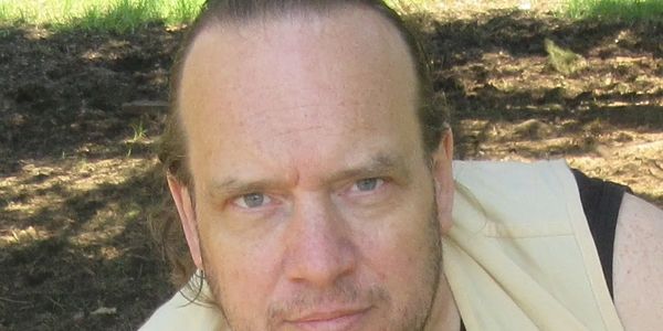 Man with light hair resting his chin on his hand outdoors.