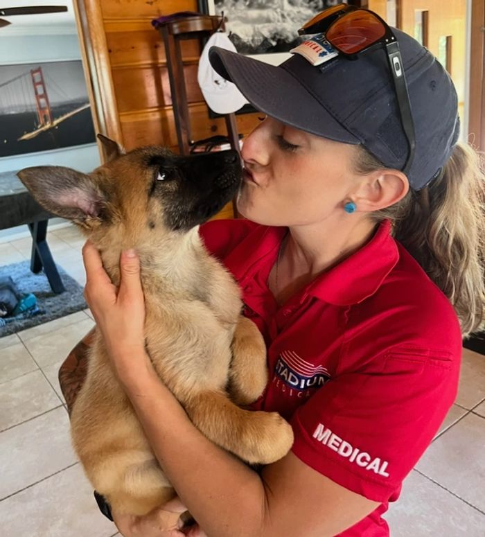 Woman in red shirt lovingly holds and kisses a puppy indoors.