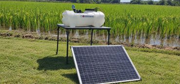 Solar panel powering a water pump in a field.