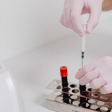 Gloved hands drawing blood with syringe from vial.