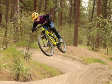 A person wearing a yellow helmet jumps with a mountain bike on a dirt trail.