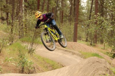 A cyclist wearing a helmet jumps on a dirt trail in the forest.
