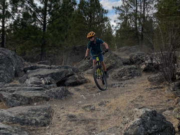 A child mountain biking on a rocky trail in a forest.