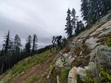 Mountain biker descending a rocky trail in a forested area.