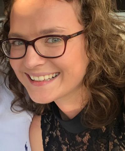 Smiling woman with curly hair and glasses.