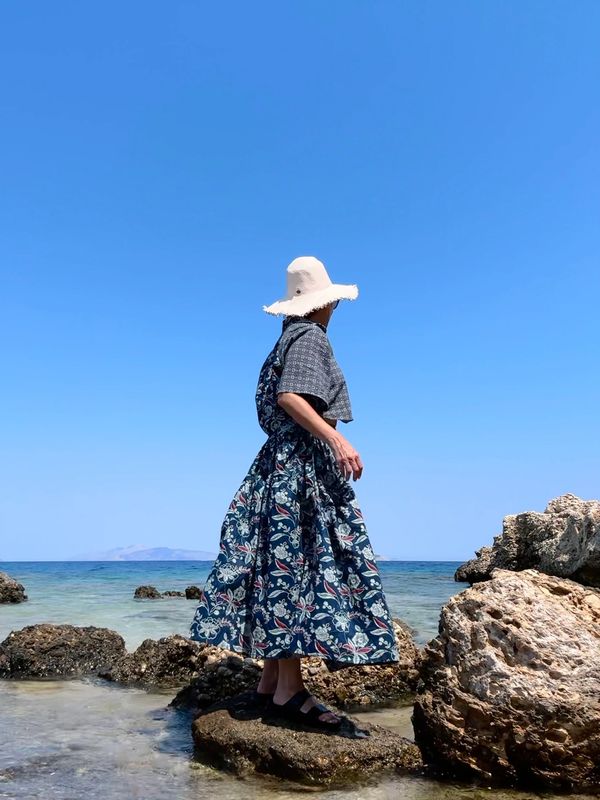 Woman looking at the Aegean standing on the rocky shore of a greek island