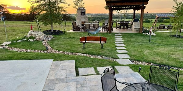 A backyard patio with seating, a fireplace, and a sunset view over green fields.