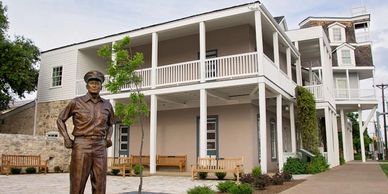 Statue of a man in uniform in front of a two-story white building with benches.