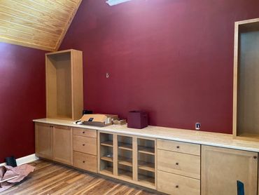 Unfinished wooden cabinetry against a burgundy wall in a room with wooden floor.