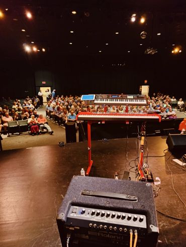 View from stage showing keyboard and audience in theater.
