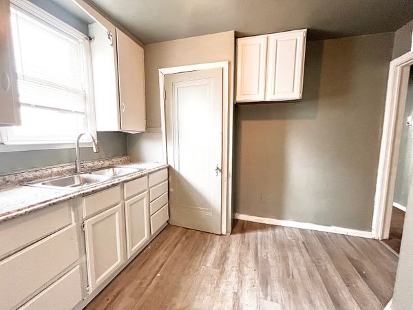 Empty kitchen with white cabinets and wood flooring.