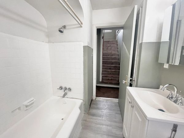 Simple bathroom with white bathtub, sink, and gray walls leading to a stairway.