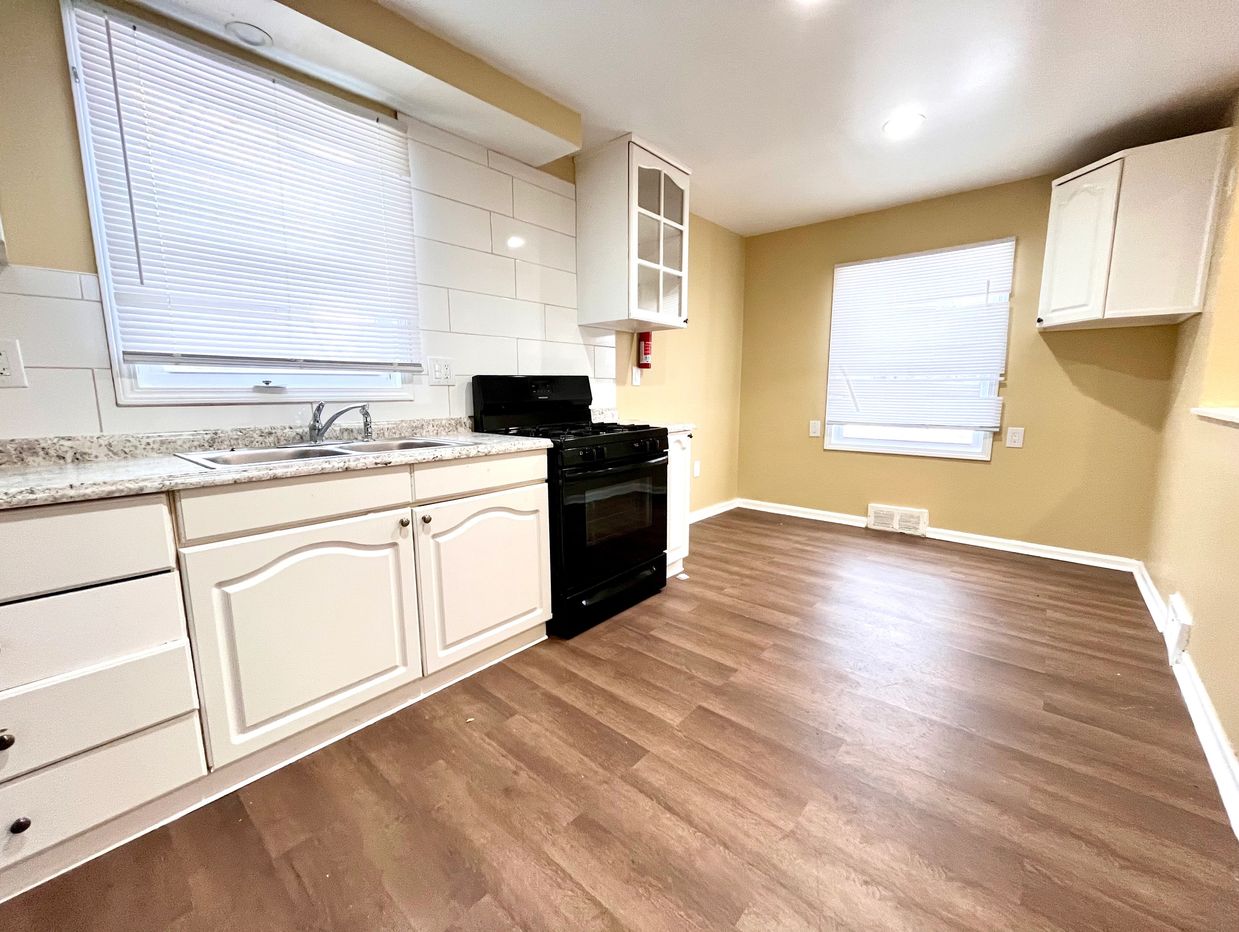 Bright kitchen with white cabinets, black stove, and wood flooring.