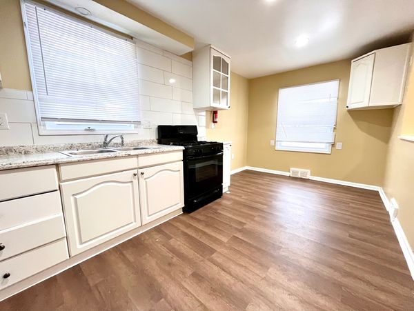 Bright kitchen with white cabinets, black stove, and wood flooring.