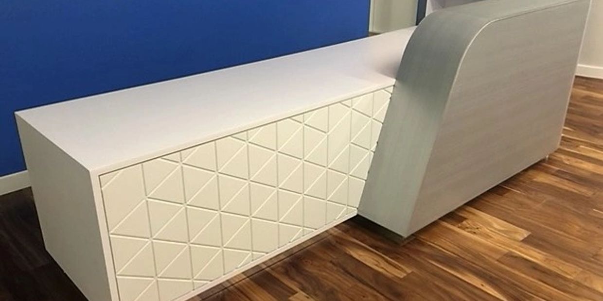 Modern white cabinet with geometric patterns on a wooden floor against a blue wall.