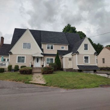 Large beige house with dark roof under cloudy sky.