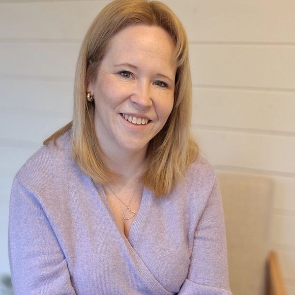 Smiling woman in a lavender sweater sitting comfortably on a chair.