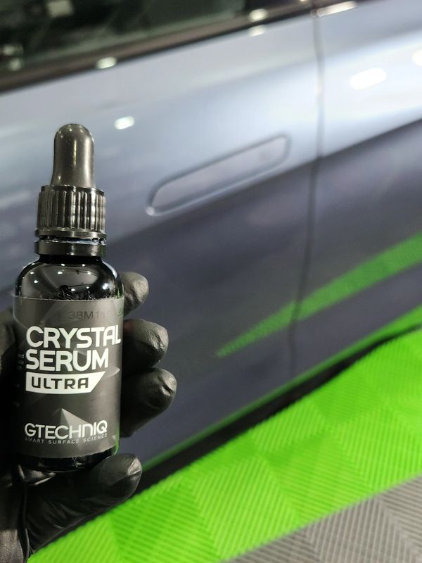 Hand holding Gtechniq Crystal Serum Ultra bottle near a car door.