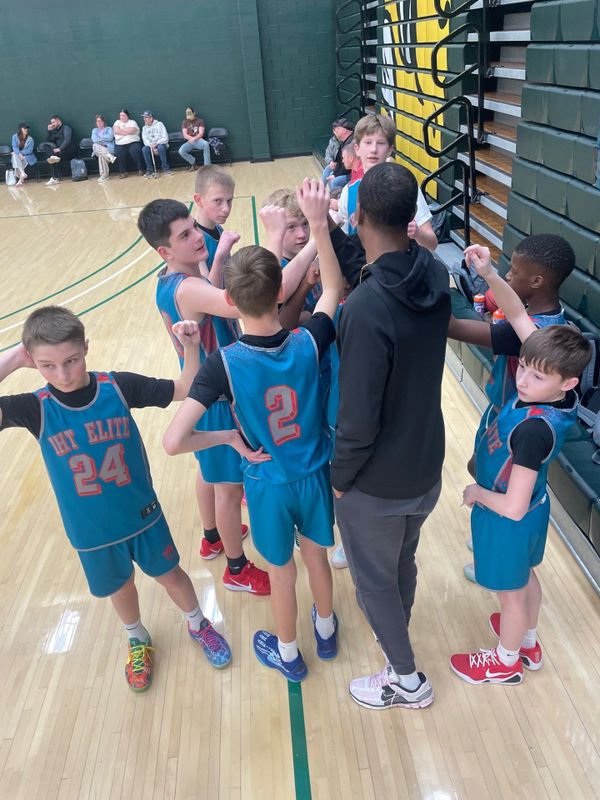 Youth basketball team huddles with coach for a motivational cheer.