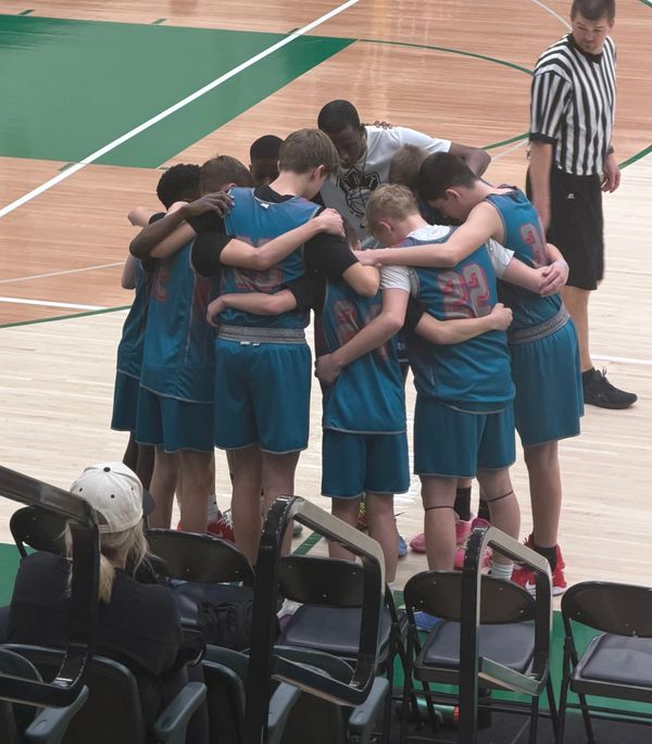 Youth basketball team huddled together on the court before the game starts.