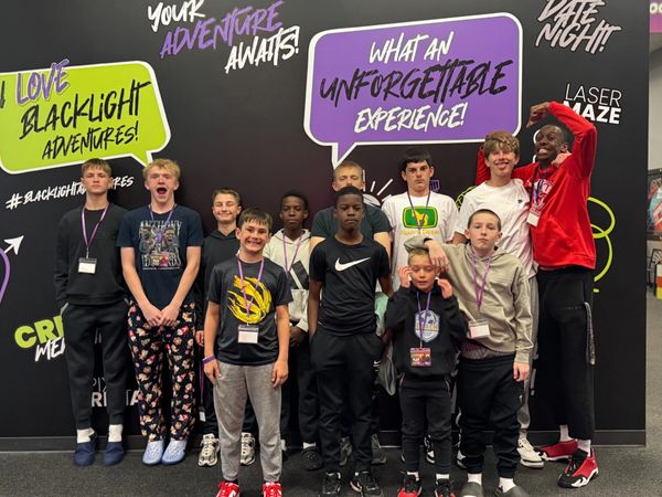 Group of boys posing in front of colorful black-light adventure signs indoors.