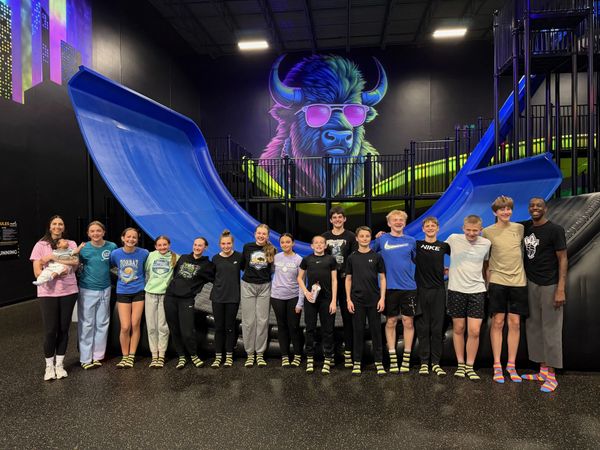 Group of teenagers posing inside a trampoline park with a colorful buffalo mural.