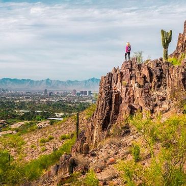 A person standing on a rocky cliff overlooking a city and desert landscape.