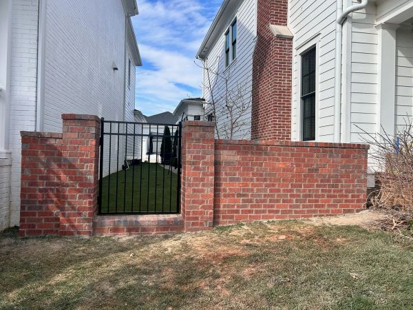 Brick fence with black metal gate between houses.