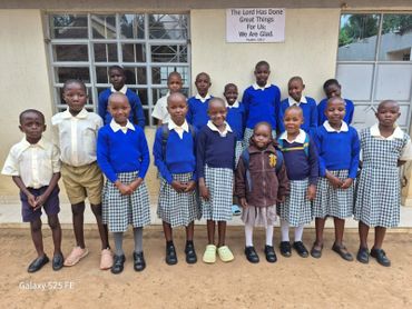 Group of school children in uniforms posing outside a building.