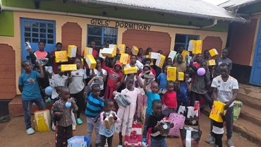 Group of children holding gifts outside a girls' dormitory building.