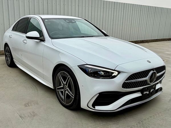 White Mercedes-Benz sedan parked on concrete near a corrugated metal fence.