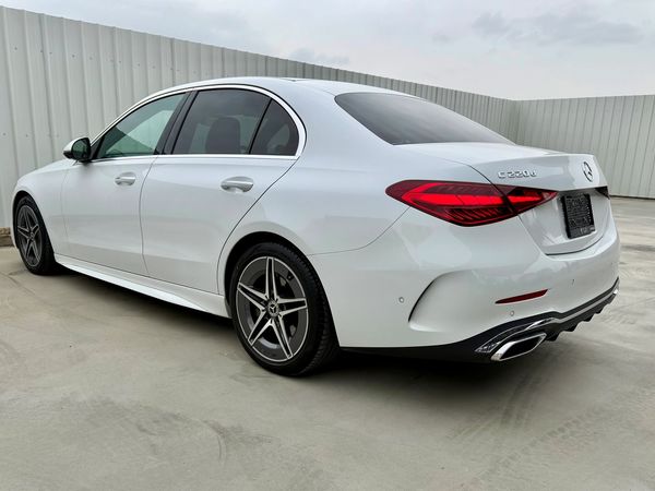 White Mercedes-Benz C-Class sedan parked on concrete near metal fencing.