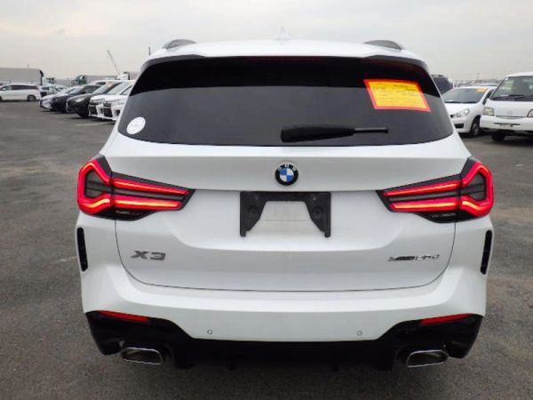 Rear view of a white BMW X3 with illuminated tail lights in a parking lot.