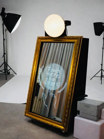 A golden-framed interactive mirror with 'Touch Here to Start' text in a studio setup.