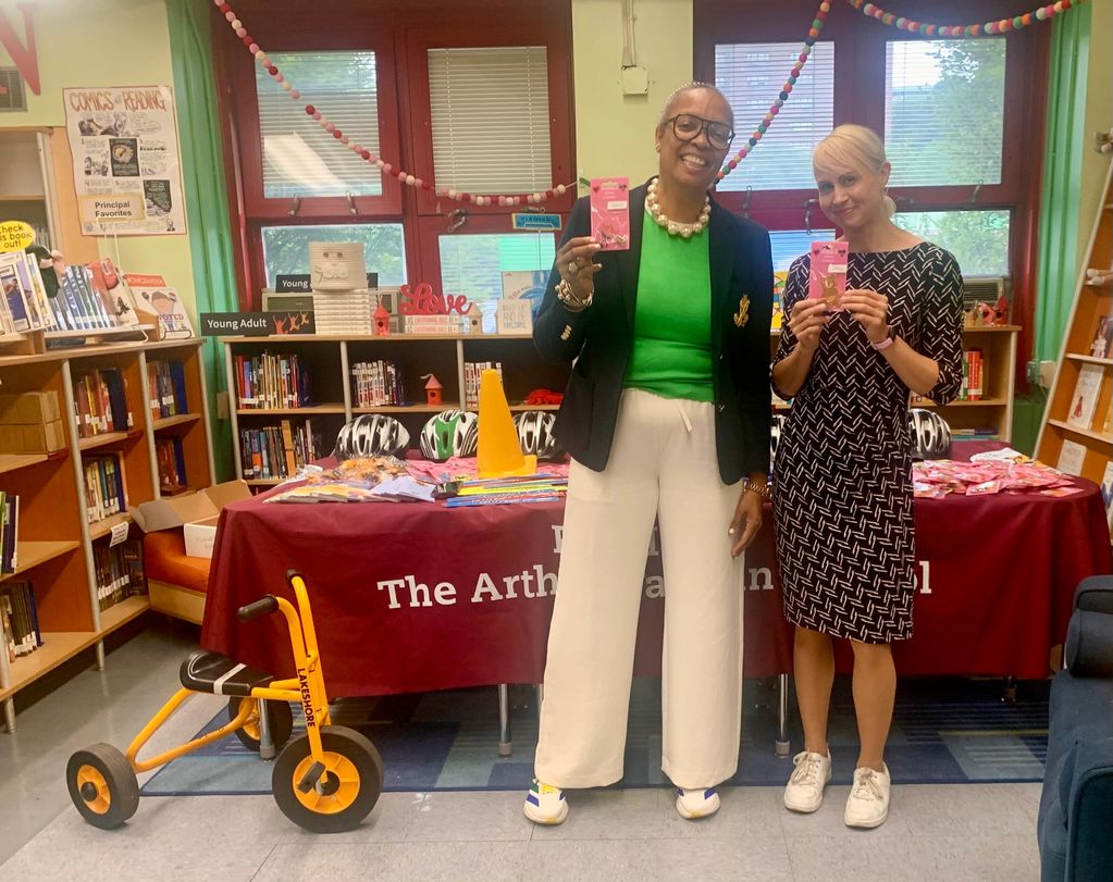 Two women holding items standing in a school library.