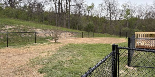 A fenced grassy area with a dirt path and trees in the background.