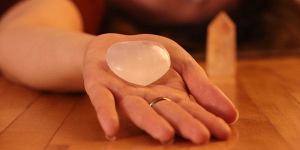 Hand holding a polished, translucent heart-shaped stone on a wooden surface.
