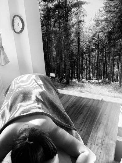 Person lying face down on a massage table under a blanket in a room with a forest mural.