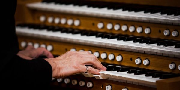 Close-up of hands playing a multi-tiered organ keyboard.