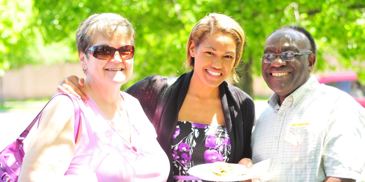 Three smiling people posing outdoors on a sunny day.