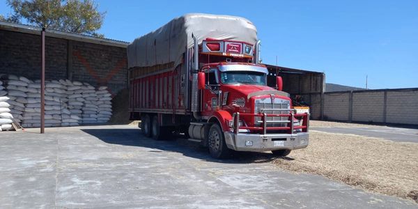 A red truck parked near stacked sacks in an industrial yard on a sunny day.