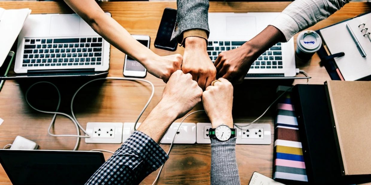 Four people fist bumping over a desk with laptops, symbolizing teamwork.