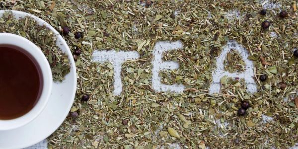 A cup of tea next to loose tea leaves spelling 'TEA'.