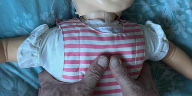 Hands performing chest compressions on an infant CPR training doll.