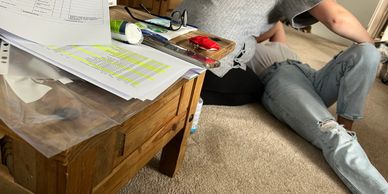 Person lying on carpet near a wooden table with papers and glasses.